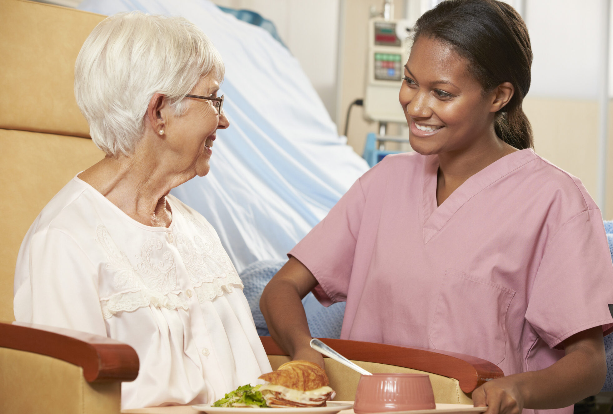 Nurse Serving Meal To Senior Female Patient Sitting In Chair