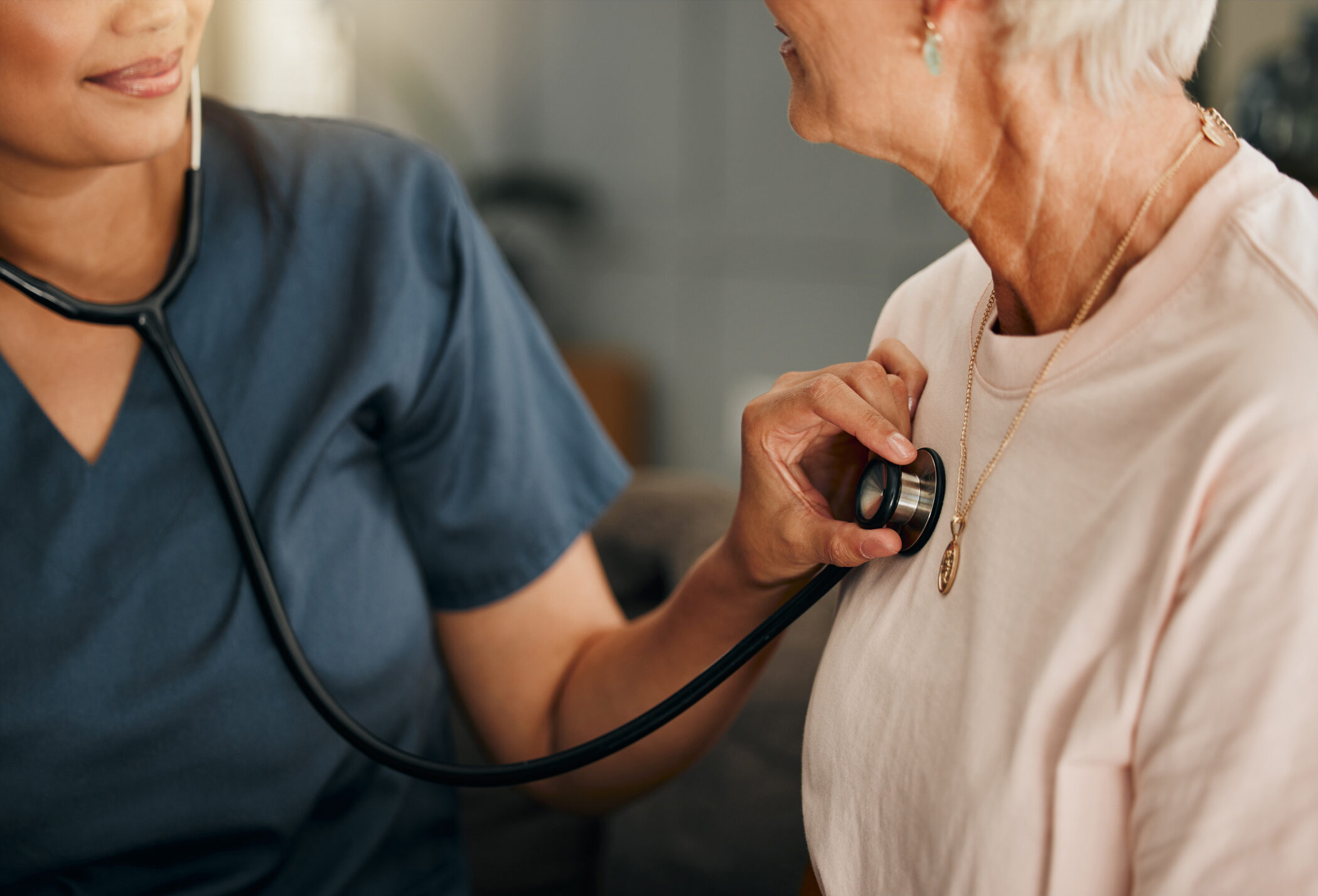 Cardiology consultation, doctor and senior woman consulting about healthcare on living room sofa in retirement home. Hand of nurse with stethoscope while helping elderly patient with medical service